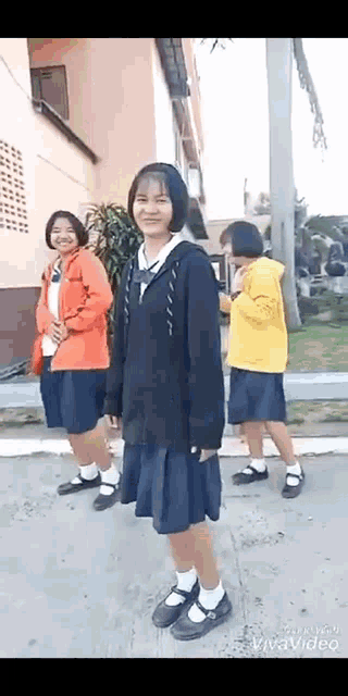 a group of young girls in school uniforms are standing on a sidewalk in front of a building .
