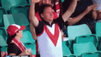 a man in a red and white jersey is standing in a stadium with his arms in the air .