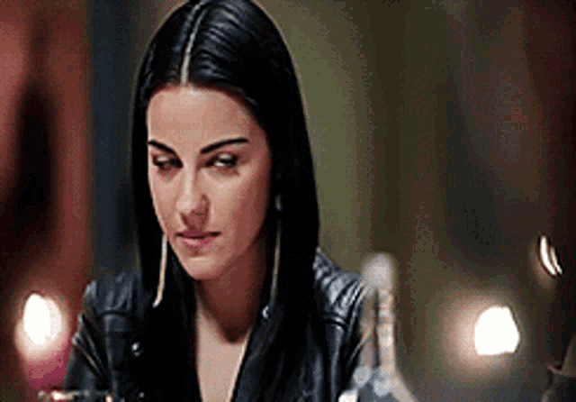 a woman in a leather jacket is sitting at a table in a dark room .