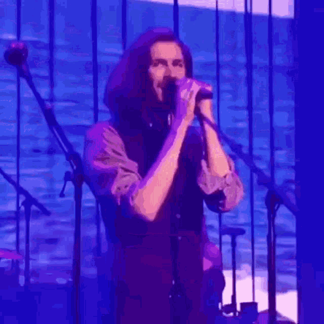 a man is singing into a microphone on a stage in front of a ocean .