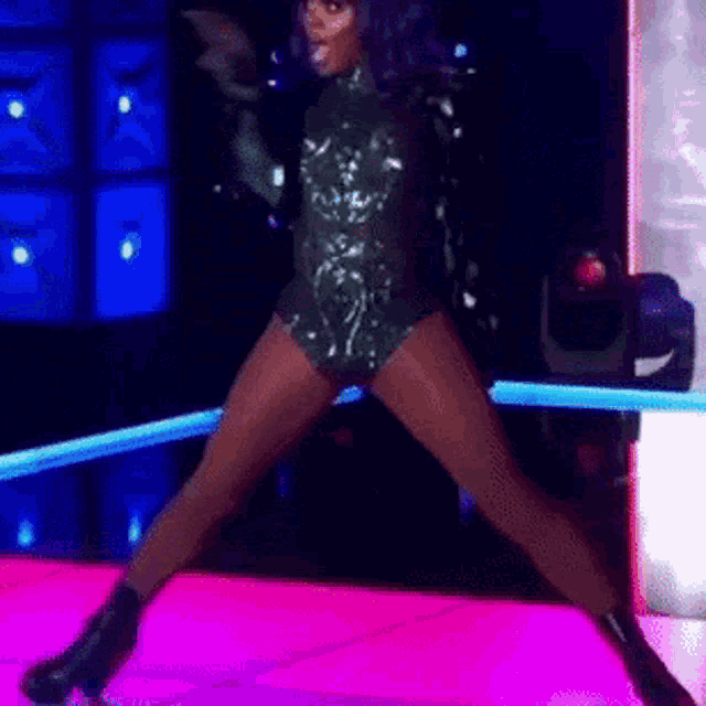 a woman in a black bodysuit is dancing on a stage with a purple background .