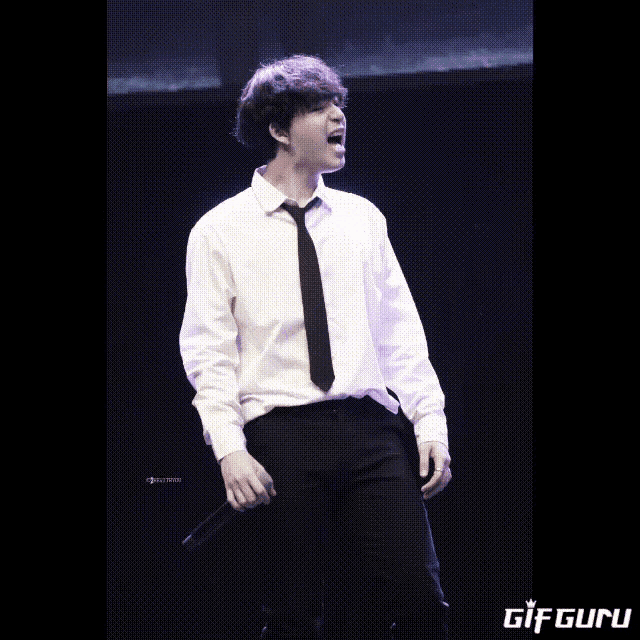 a man in a white shirt and black tie is singing into a microphone with a gif guru logo behind him
