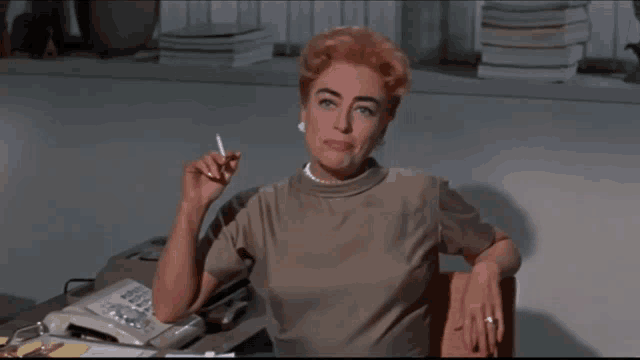 a woman sits at a desk holding a cigarette
