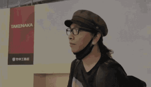 a man wearing glasses and a hat is standing in front of a sign that says takenaka
