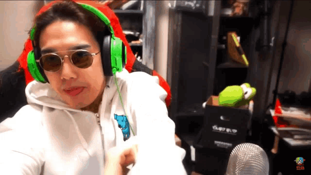 a man wearing headphones and sunglasses is sitting in front of a microphone and a box that says ' supreme '