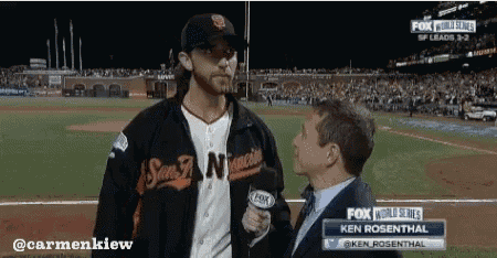 a man in a san francisco giants jacket is being interviewed by a man in a suit