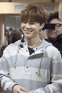 a young man wearing a striped hoodie is smiling while standing in front of a camera .