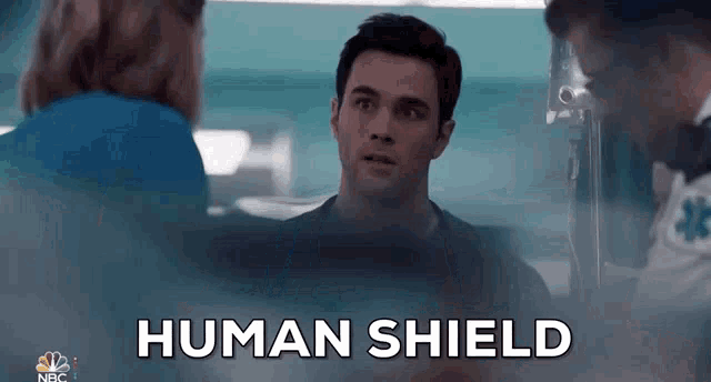 a man is talking to two nurses in a hospital room and the words human shield are visible .