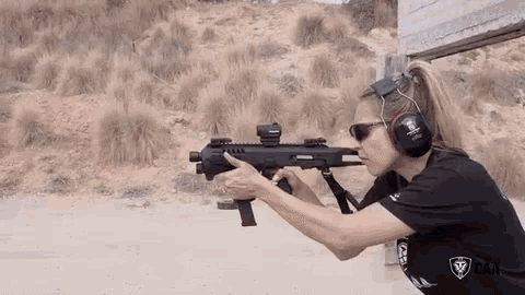 a woman is holding a gun and pointing it at a target .
