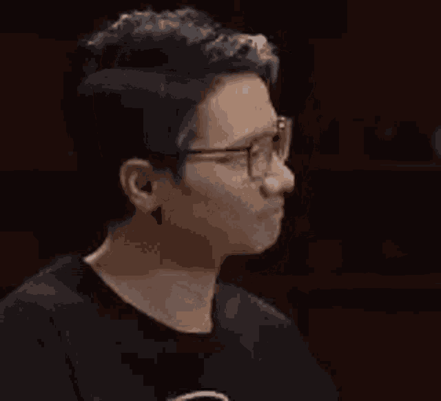 a man wearing glasses and a black shirt is looking down at something .
