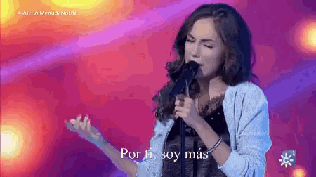 a woman singing into a microphone with the words por ti soy mas written below her