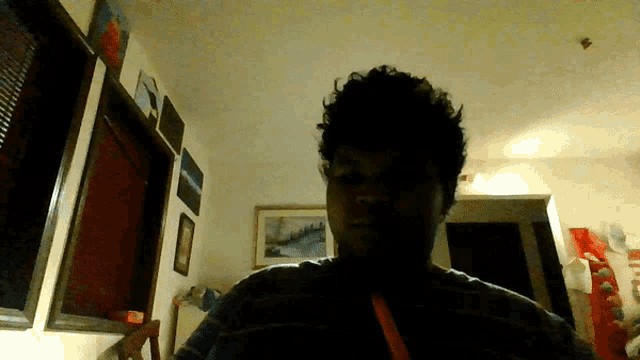 a man with curly hair is standing in a dark room with a picture on the wall