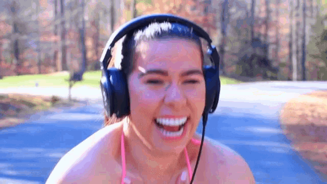 a woman in a bikini is wearing headphones and smiling while walking down a road .