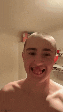 a young man with a shaved head is making a funny face with his tongue out .