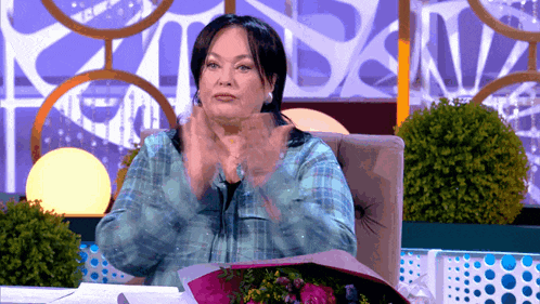 a woman is sitting in a chair with a bouquet of flowers and clapping her hands
