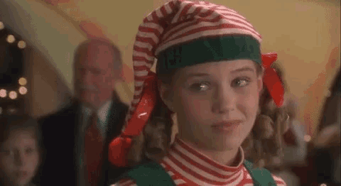 a girl is dressed as an elf and wearing a striped hat and striped shirt .