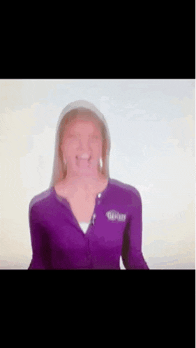 a woman in a purple jacket is smiling while standing in front of a white background .