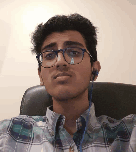 a man wearing glasses and ear buds looks at the camera