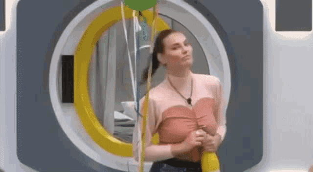 a woman in a pink top is standing in front of a camera holding a balloon .
