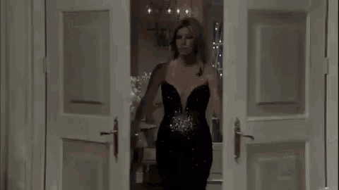 a woman in a black dress is standing in a doorway holding a clutch .