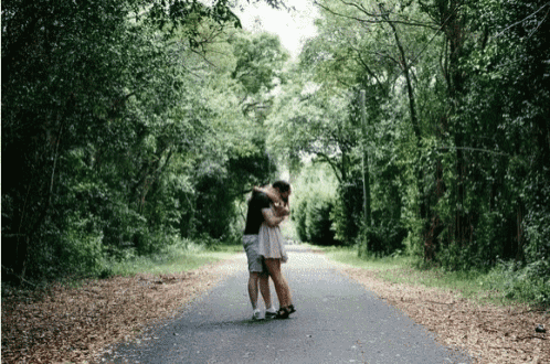 a man and a woman are hugging on a road in the woods