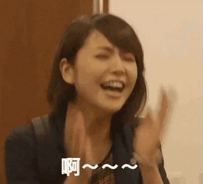 a woman is laughing and clapping her hands in front of her face .