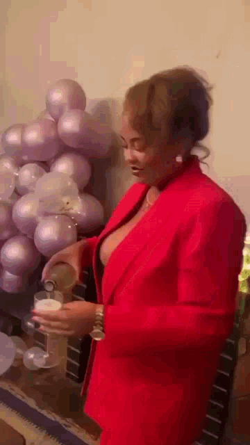 a woman in a red jacket is standing in front of balloons and holding a glass of wine .