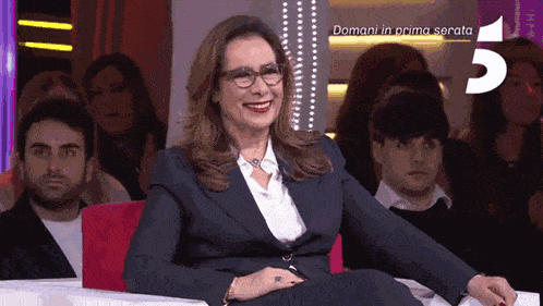 a woman in a suit and glasses sits in front of a crowd with the words domani in prima serata on the bottom