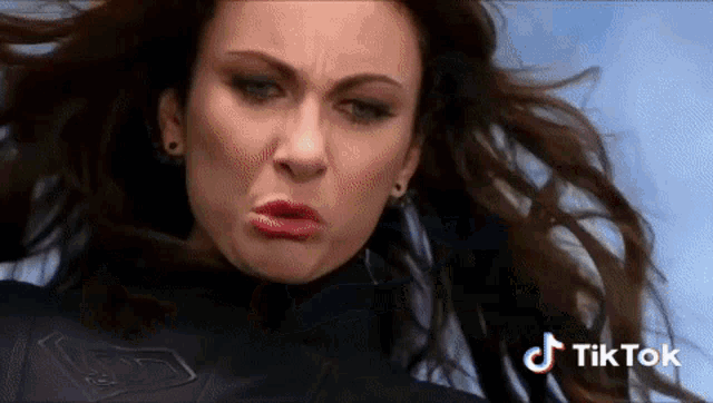 a close up of a woman making a funny face with her hair blowing in the wind