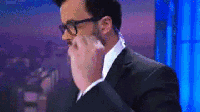 a man in a suit and glasses is covering his face with his hands .