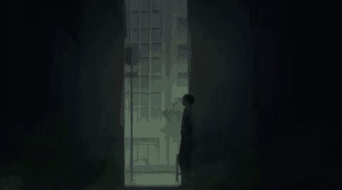 a person is sitting in a chair in a dark room looking out a window .