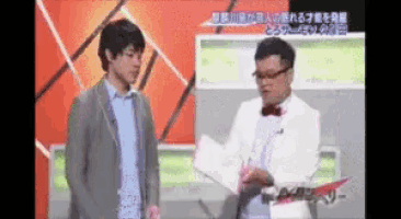 two men are standing next to each other on a tv show and one of them is holding a piece of paper