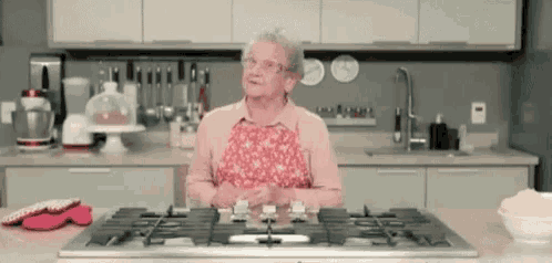 an elderly woman in a pink apron is standing in a kitchen