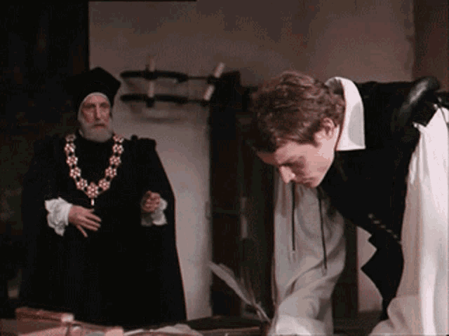 a man with a necklace of flowers is standing next to a man in a black robe