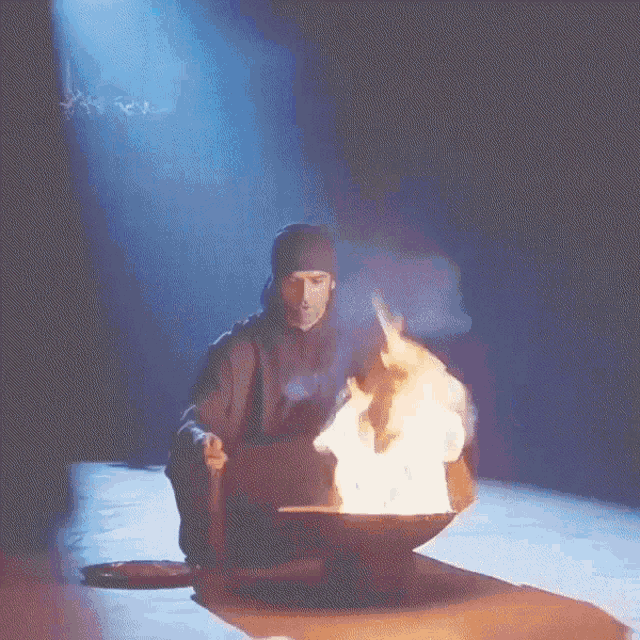 a man sitting in front of a bowl of fire with smoke coming out of it