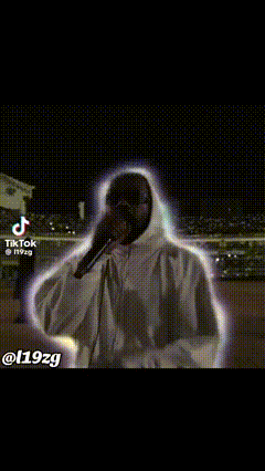 a man in a hoodie is singing into a microphone in a dark room .