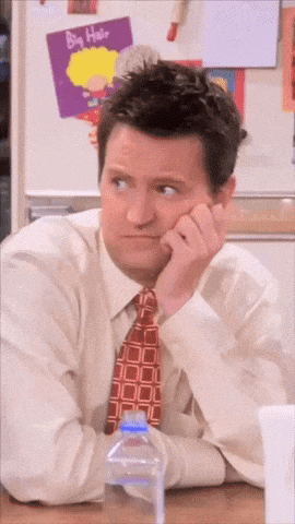 a man in a tie sits at a desk in front of a refrigerator with a big hair poster on it