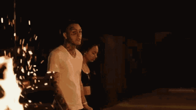a man and a woman standing next to each other in front of a fire at night .