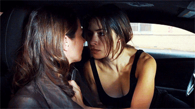 two women in a car looking at each other with a sign in the background that says no parking