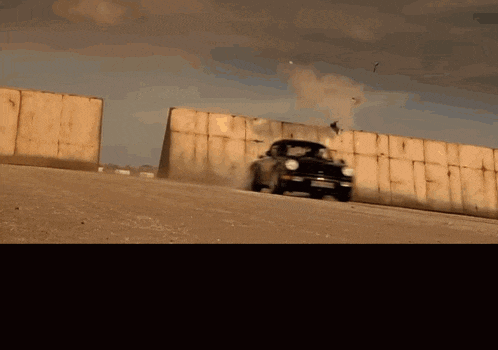 a car is driving down a dirt road near a wall