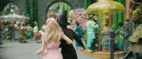a woman in a pink dress is walking with a witch in a black costume