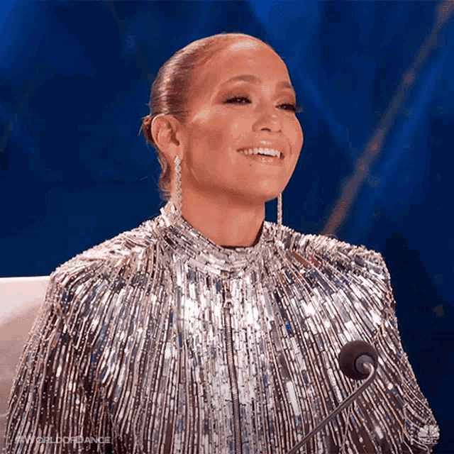 a woman wearing a silver sequined dress is smiling in front of a microphone
