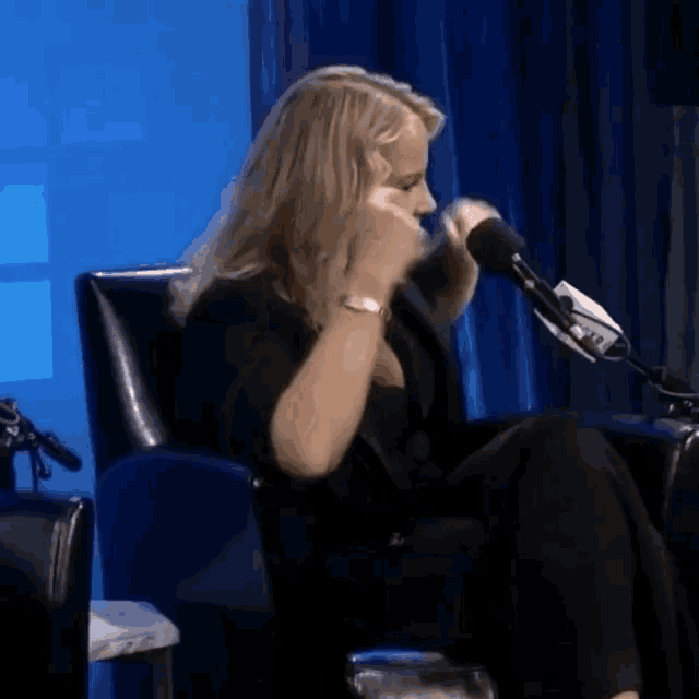 a woman is sitting in front of a microphone and covering her mouth with her hands