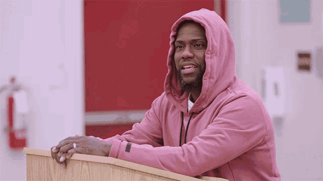 a man in a pink hoodie is leaning on a wooden podium