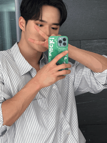 a man in a striped shirt is taking a picture of himself with a green case that says tncr