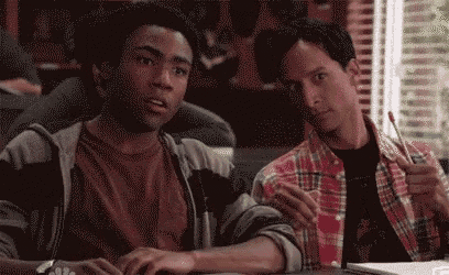 two men are sitting at a table looking at a computer screen . one of the men is giving a thumbs up .