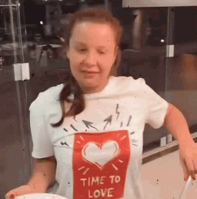 a woman wearing a t-shirt that says `` time to love '' is cooking in a kitchen .