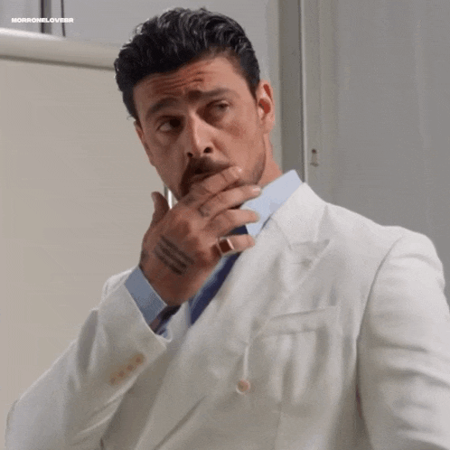 a man in a white suit and tie is covering his mouth with his hand