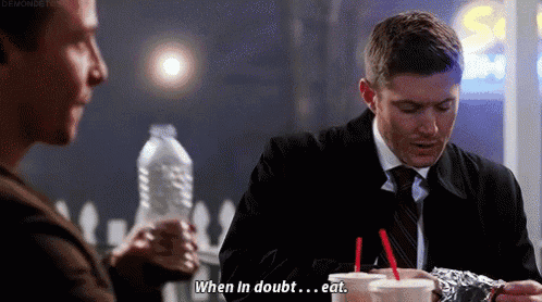 a man in a suit and tie is sitting at a table with a bottle of water and drinking a milkshake .