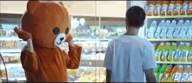 a man in a teddy bear costume stands in front of a refrigerated section of a store ..